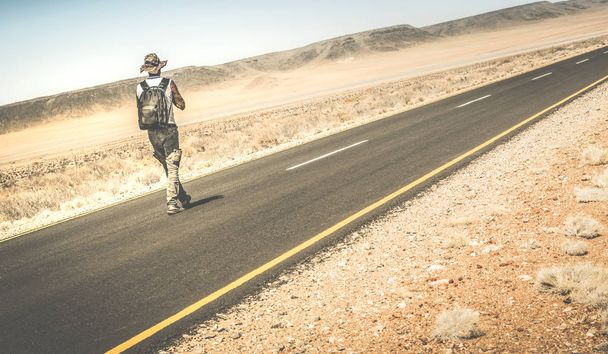 Férfi sétál az úton, a Namíbiai afrikai sivatagban - alternatív életmód fogalma és tapasztalat mehetnék srác hátizsákkal ismeretlen - Travel utazás kaland a világ - Retro szűrő - Fotó, kép