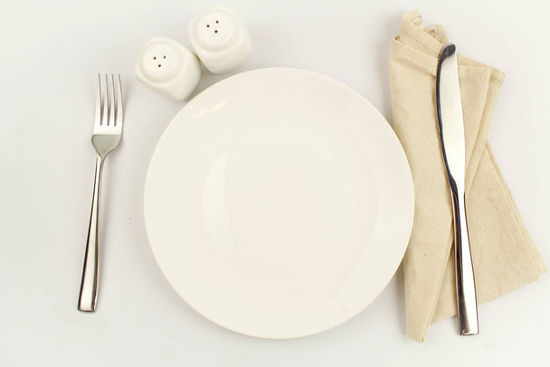 άσπρο πιάτο σε λευκό φόντο διακόσμηση με κουτάλι και πιρούνι - Φωτογραφία, εικόνα
