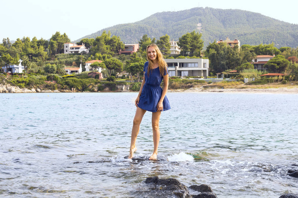 Pretty young woman standing on the stone in the sea and laughing - Foto, Imagen