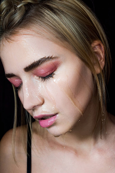 Seductive blonde with beautiful make-up. Pink shade, beauty portrait of a sexy girl. A tender girl. Beautiful girl with a gentle make-up. The girl transparent liquid dripping down her face. - Photo, Image