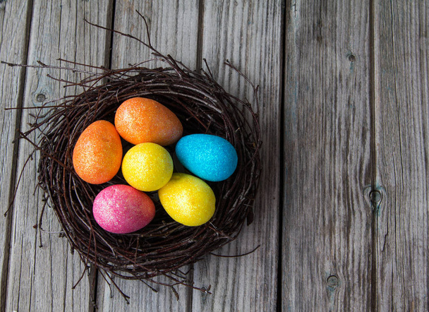 gekleurde eieren liggen in een nest op een grijze houten achtergrond - Foto, afbeelding