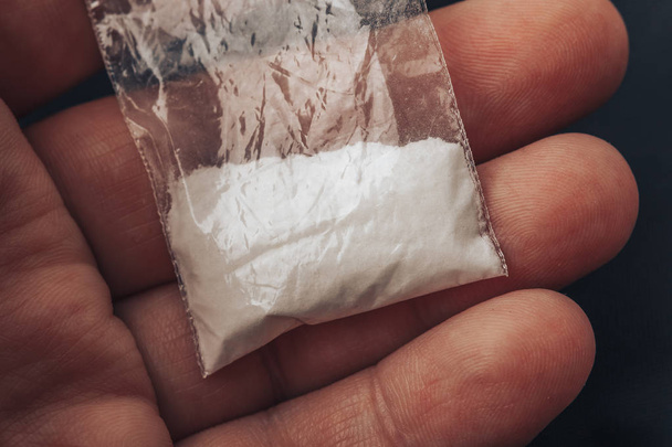 Kunststof packet met cocaïnepoeder of een andere drugs in mans hand. Close-up macro - Foto, afbeelding