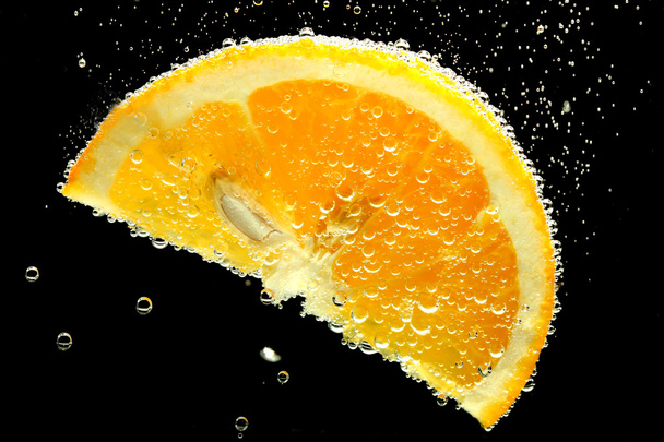 slice of orange in the water with bubbles, on black background - Photo, Image