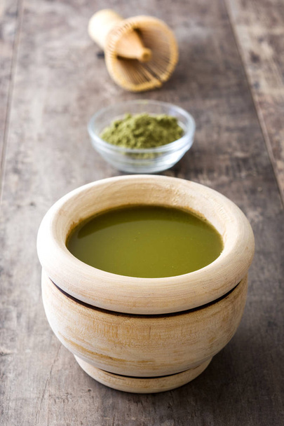 Té verde matcha en un tazón y batidor de bambú, sobre fondo de madera
 - Foto, imagen