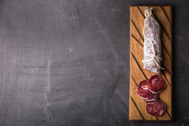 Fresh salami on a vintage Board. Vintage Cutlery fork and knife on a black coated background. Copy space. - Zdjęcie, obraz