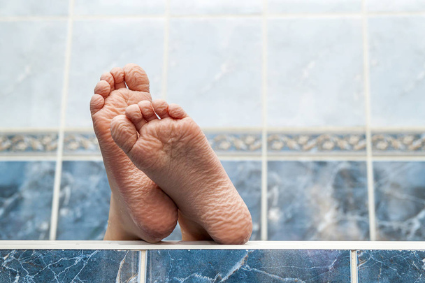 Wrinkled bare feet coming out from a bathtub. Young person getti - Photo, image