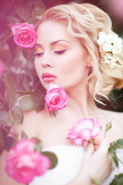 Beautiful Brunette Bride near a Flowering Bush Roses Posing in a Wedding Dress - Фото, изображение