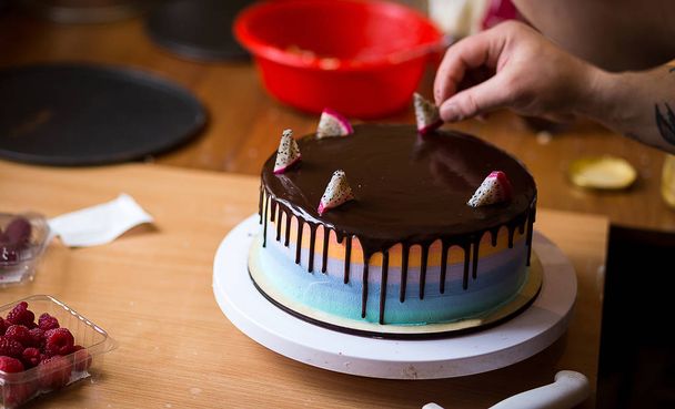 Banketbakker in de keuken versieren van een taart van chocolade, fruit, snoep, snoep is het versieren van chocoladetaart, kooklessen, culinaire, bakkerij, voedsel en mensen concept - Foto, afbeelding