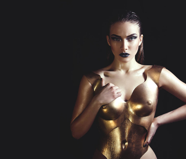 The girl in a gold metal corset in the studio on a black background. - Фото, изображение