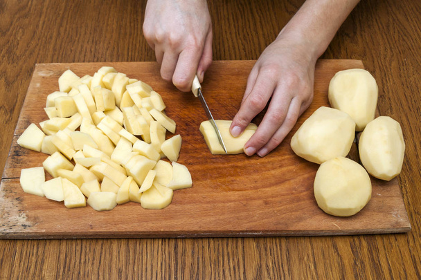 Woman's hand with a knife cutting slicing potatoes on wooden boa - Foto, imagen