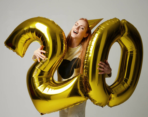 Young happy girl with huge gold digit twenty balloons as a prese - Fotó, kép