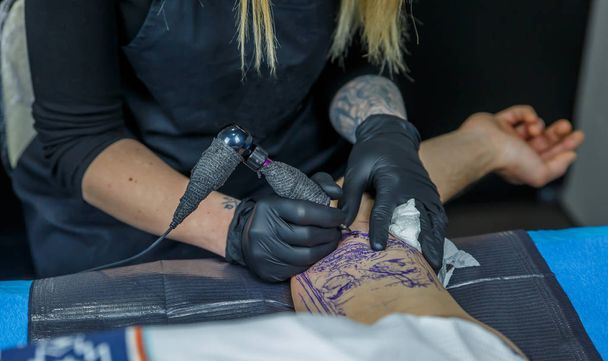 Une fille blonde tatoueuse dessine un tatouage avec sa machine à tatouer
 - Photo, image