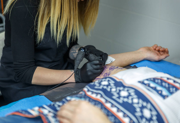 Blondi taiteilija tyttö kiinnittää neulalla tatuointi käsivarteen
  - Valokuva, kuva