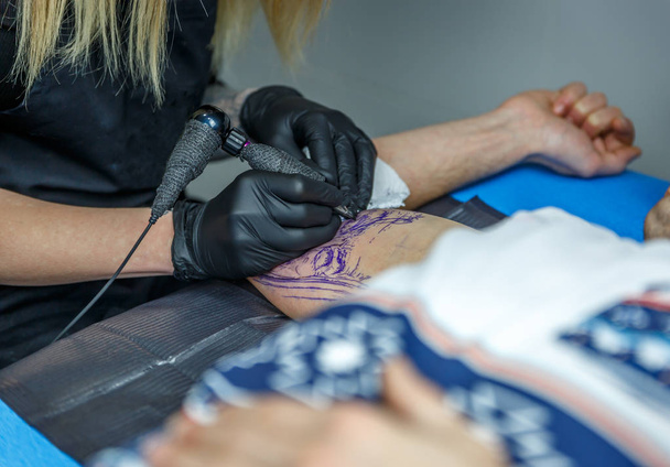 Una artista tatuadora tatuando un brazo con cuidado
 - Foto, Imagen
