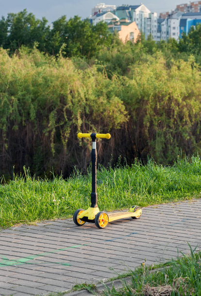 Kolmipyörän säädettävä korkeus keltainen skootteri polulla päällystys laatat kaupungin puistossa
 - Valokuva, kuva