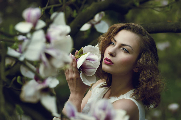 Retrato de una hermosa joven (niña) con el pelo ondulado rubio y delicados rasgos en el fondo de un árbol de magnolia floreciente. El concepto de "la llegada de la primavera". Disparando al aire libre. Luz del día
 - Foto, imagen