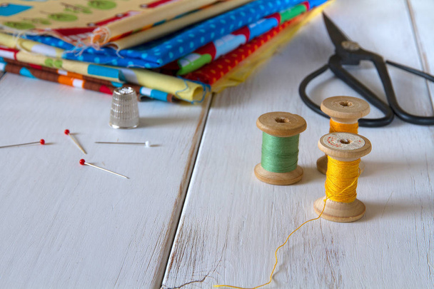 Colorful fabrics with vintage scissors, pins, measuring tape and rolling cotton threads on white wooden table - Photo, image