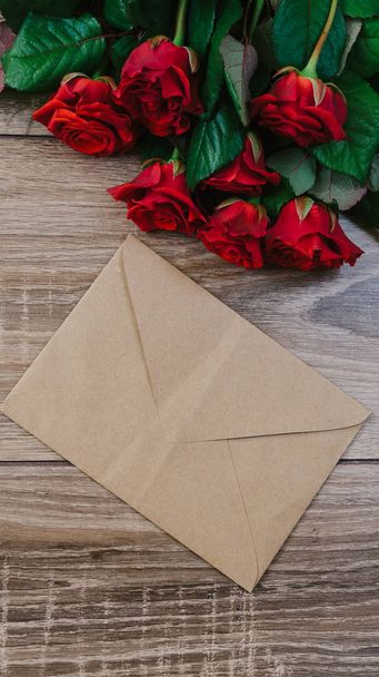 Buquê de rosas vermelhas em uma mesa de madeira com um envelope e um cartão de papel em branco para o seu texto
 - Foto, Imagem