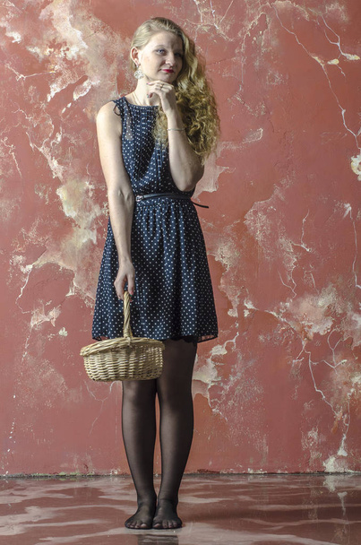 Young girl with blonde curly hair in a long dress with polka dots and stockings dancing with a basket - Foto, Imagen