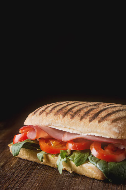French baguette with sausage, tomatoes and lettuce. Dark backgro - Photo, image
