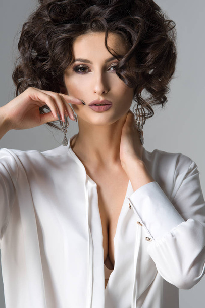 Sensual beautiful brunette woman posing in white shirt and earrings. Girl with long curly hair.  - Φωτογραφία, εικόνα