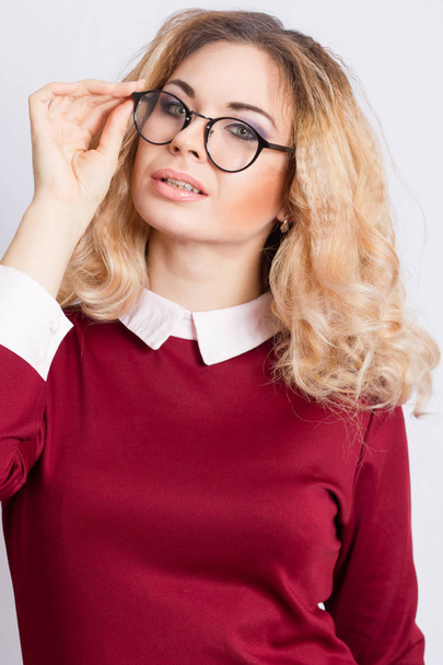 Portrait of beautiful caucasian blonde woman with curly hair standing on grey background. Young business woman with glasses looking at camera - Foto, imagen
