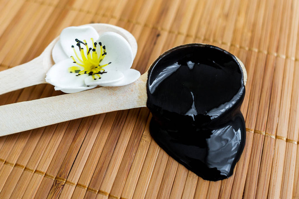 Bambu bir arka plan üzerine bir tahta kaşık içinde siyah bir madde. Siyah maske - Fotoğraf, Görsel