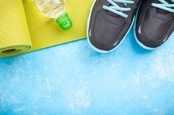 Mata do jogi, buty sportowe i butelka wody na niebieskim tle. Pojęcie zdrowego stylu życia, sportu i diety. Sprzęt sportowy - Zdjęcie, obraz