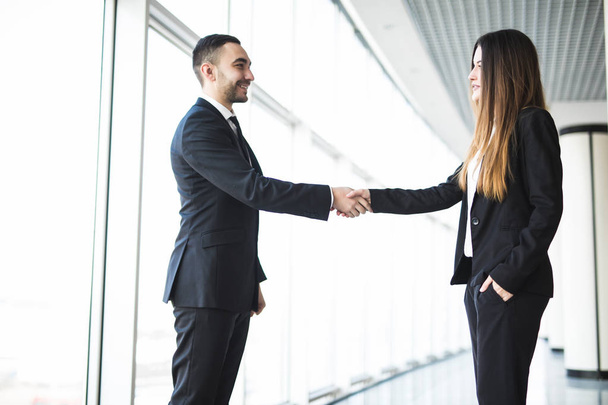 Бизнесмен и предпринимательница пожимают руки в офисе с большими панорамными окнами
 - Фото, изображение