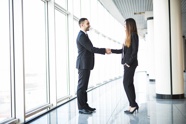 Бизнесмен и предпринимательница пожимают руки в офисе с большими панорамными окнами
 - Фото, изображение
