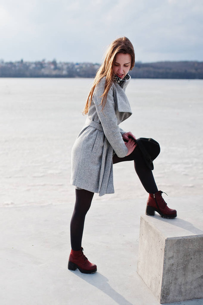 Young model girl in gray coat posed on stone cube against freeze - Fotó, kép
