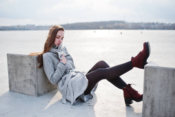 junges Model-Mädchen im grauen Mantel posierte sitzend in der Nähe von Steinwürfel agai - Foto, Bild