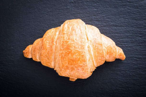 Čerstvý croissant na černém břidlicovém pozadí. Horní pohled - Fotografie, Obrázek