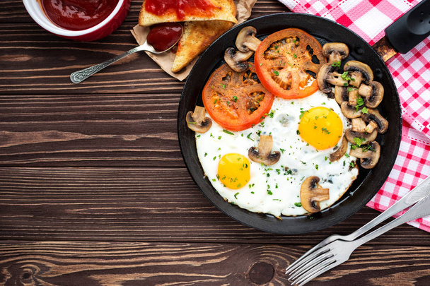 Huevos fritos con champiñones y tomate sobre mesa de madera oscura
  - Foto, imagen