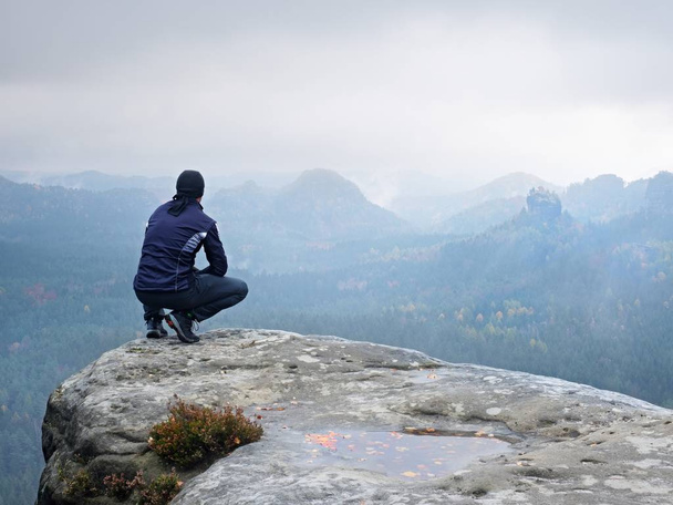 Turystycznych w czarny siedzieć na krawędzi urwiska, patrząc na mgliste doliny pagórkowaty - Zdjęcie, obraz