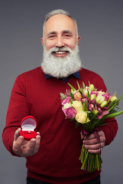 Зрілий бородатий чоловік робить пропозицію з обручкою заручин і буком
 - Фото, зображення