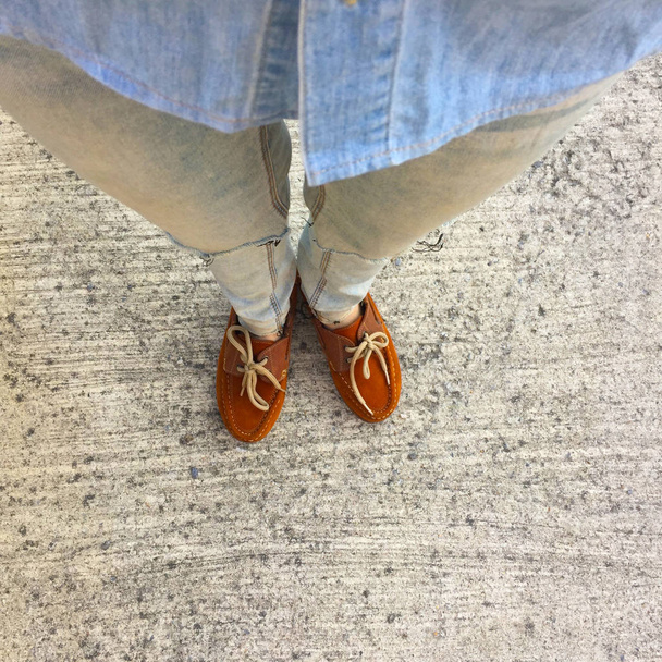 Mavi Jeans ve beton zemin üzerinde kahverengi ayakkabı kadının bacaklarını açıp  - Fotoğraf, Görsel