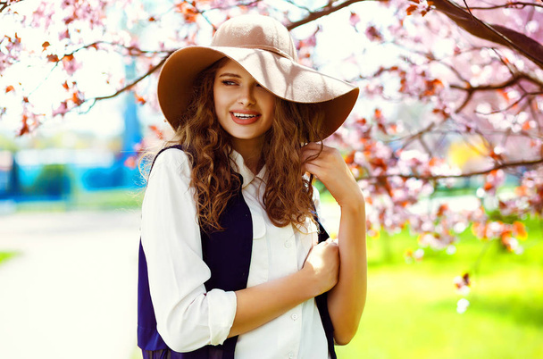Outdoor portrait of young beautiful fashionable lady posing near flowering tree. Model wearing stylish accessories & clothes. . Female beauty & fashion. - Foto, afbeelding