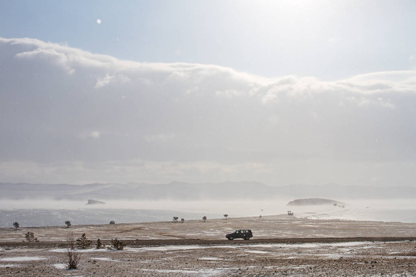 Живописный вид на берег озера Байкал зимой и черный автомобиль едет вдоль скалистого берега
. - Фото, изображение