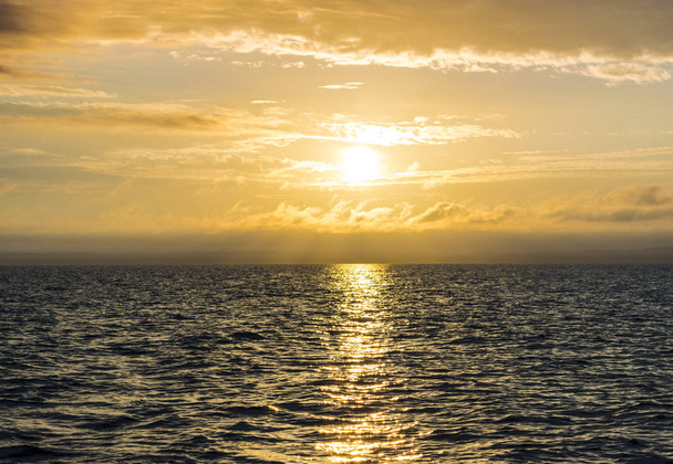 Sunset over the ocean through clouds, gold sun and sky - Фото, изображение