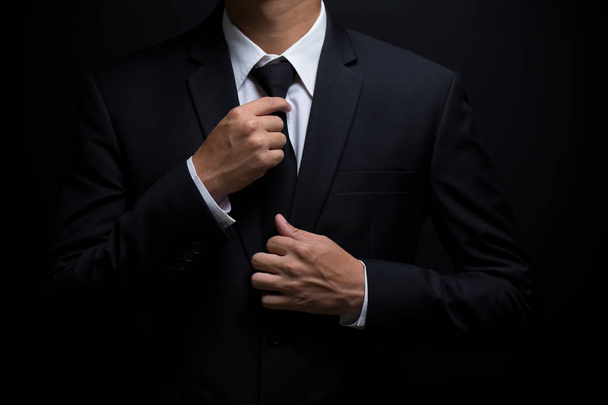 Homem de terno preto e ajustando sua gravata
 - Foto, Imagem