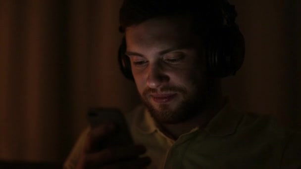 man with smartphone and headphones at night - Imágenes, Vídeo