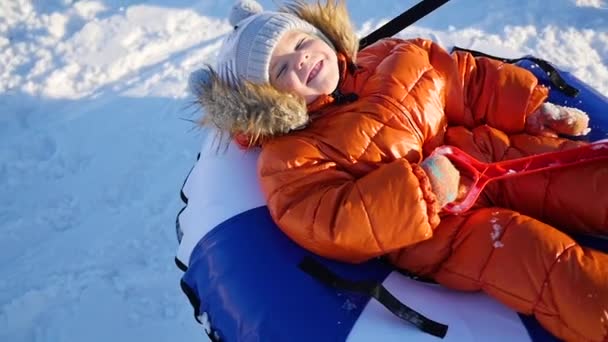 ένα χαρούμενο παιδί βόλτες μέσα snowtube σε μια αργή κίνηση χιονιού. χιόνι χειμερινό τοπίο. Υπαίθρια σπορ - Πλάνα, βίντεο
