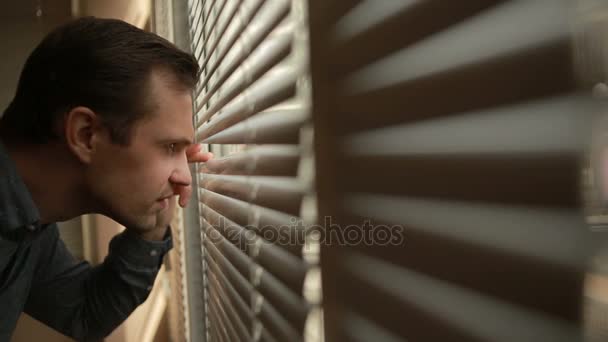 Mann schaut aus dem Fenster durch die Jalousien auf die Straße und spioniert. Verdacht - Filmmaterial, Video