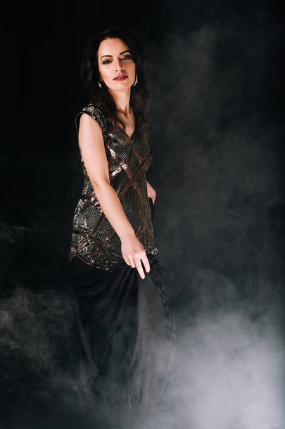 Mulher morena bonita em um vestido dançando e posando no estúdio no fundo escuro com fumaça
 - Foto, Imagem