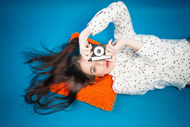 Girl with retro camera. Cheerful girl lying on the floor with her camera in hands - Фото, изображение