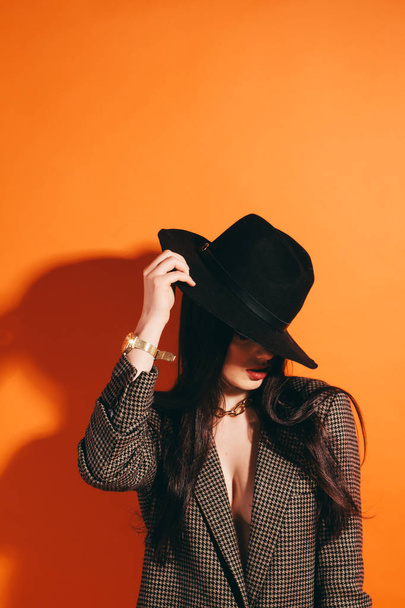 美しい少女は、茶色のジャケットでスタジオで笑います。オレンジ色の背景。帽子 - 写真・画像
