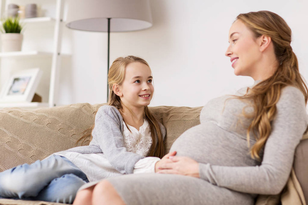 happy pregnant woman and girl on sofa at home - Photo, image