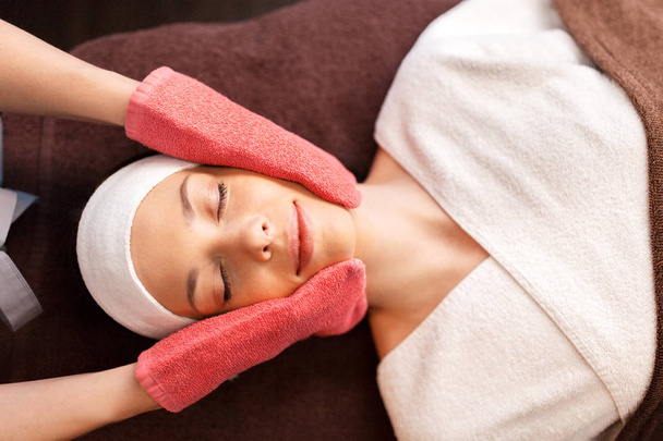 vrouw met gezicht massage met badstof handschoenen in spa - Foto, afbeelding