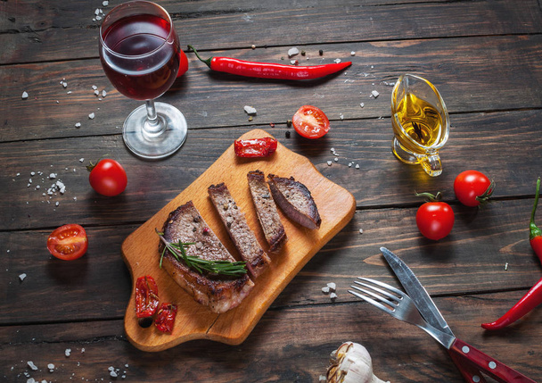 Bife grelhado temperado com especiarias servidas em uma tábua de madeira com tomate cereja fresco e pimenta vermelha
 - Foto, Imagem